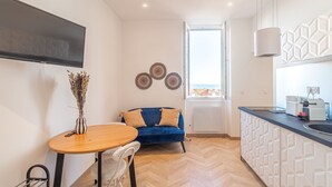 Una cocina moderna con horno empotrado, una zona de comedor con mesa y sillas de madera, un sofá azul y un ventanal grande.