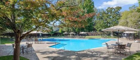 A swimming pool with a surrounding patio area, including tables and umbrellas.