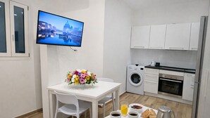 A modern kitchen with white cabinets, a washing machine, and a flat-screen TV displaying a cityscape. - Studio in the old Town of Menton (Menton)
