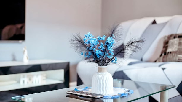 Un soggiorno moderno con un tavolino in vetro, un vaso bianco con fiori blu e un divano bianco.