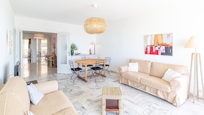A spacious living area with a wooden dining table, beige sofas, a woven coffee table, and a hanging light fixture. - Menton Garavan 2BR by the sea Parking (Menton)