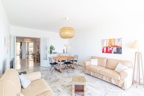 A spacious living area with a wooden dining table, beige sofas, a woven coffee table, and a hanging light fixture. - Menton Garavan 2BR by the sea Parking (Menton)