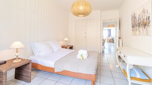 A bedroom with a bed, bedside tables, a lamp, a hanging light fixture, a painting, and a hallway leading to a living area. - Menton Garavan 2BR by the sea Parking (Menton)