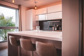 A modern kitchen with a large window, a bar area with stools, and a countertop with a glass vase. - Duplex Sea View Near Monaco AC Parking (Roquebrune-Cap-Martin)