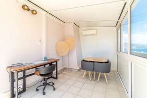 Ein kleiner Raum mit Schreibtisch, Bürostuhl, zwei runden Tischen und einem großen Fenster.