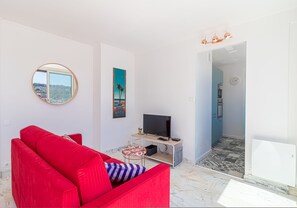 Ein modernes Wohnzimmer mit einem roten Sofa, einem Fernseher auf einem Holzboden, einem runden Spiegel und einem Gemälde.