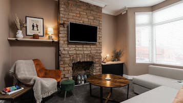 A living room with a brick fireplace, a flat-screen TV, a sofa, a coffee table, and a chair.