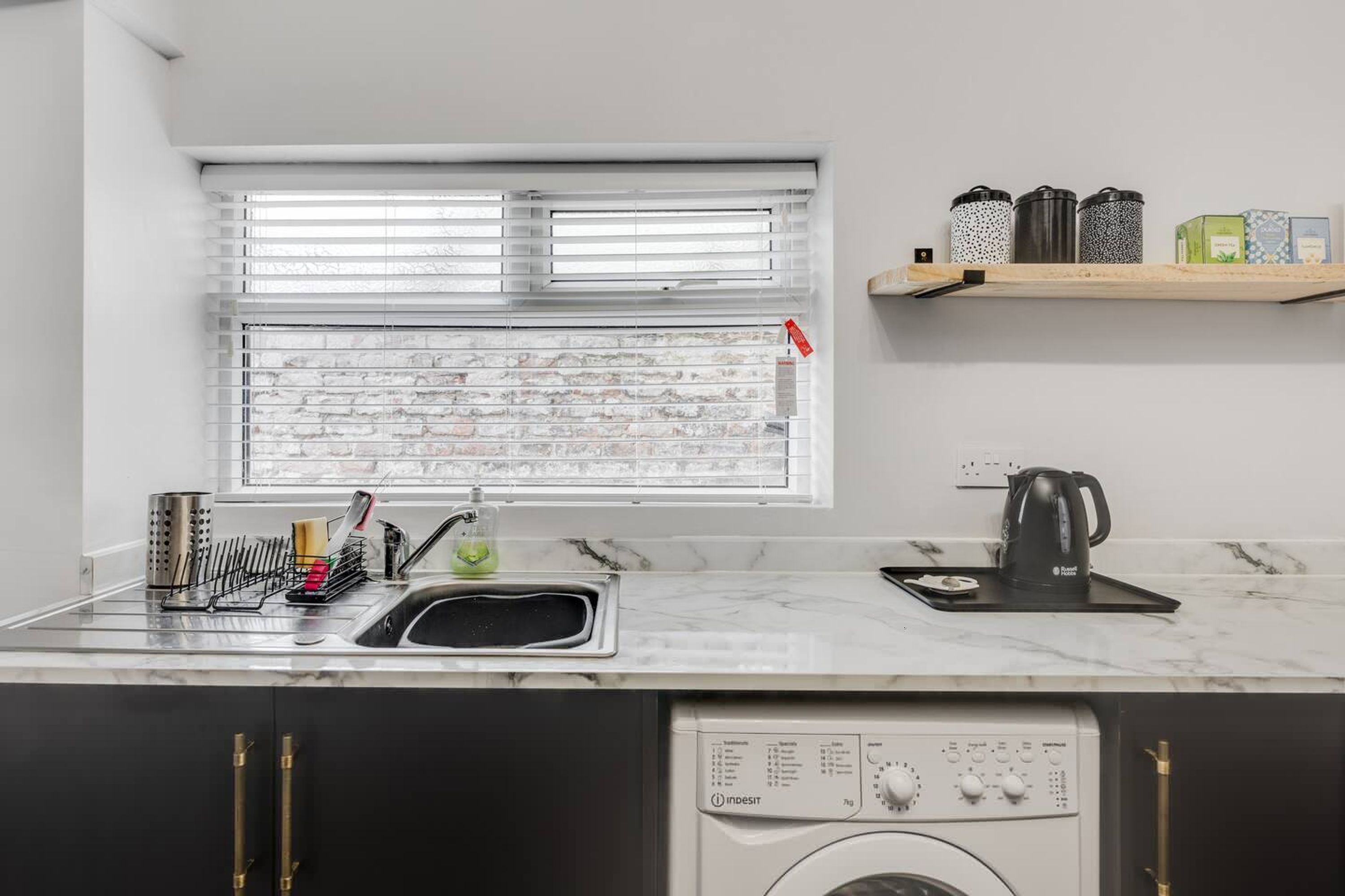A kitchen with a washing machine, a sink, and a window with blinds.