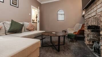A cozy living room with a sofa, a round coffee table, a stone fireplace, and a door leading to another room.