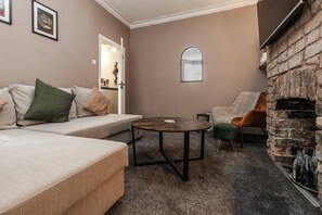 A cozy living room with a sofa, a round coffee table, a stone fireplace, and a door leading to another room. - Sefton Park 2 Desks W M Dining Parking (Liverpool)