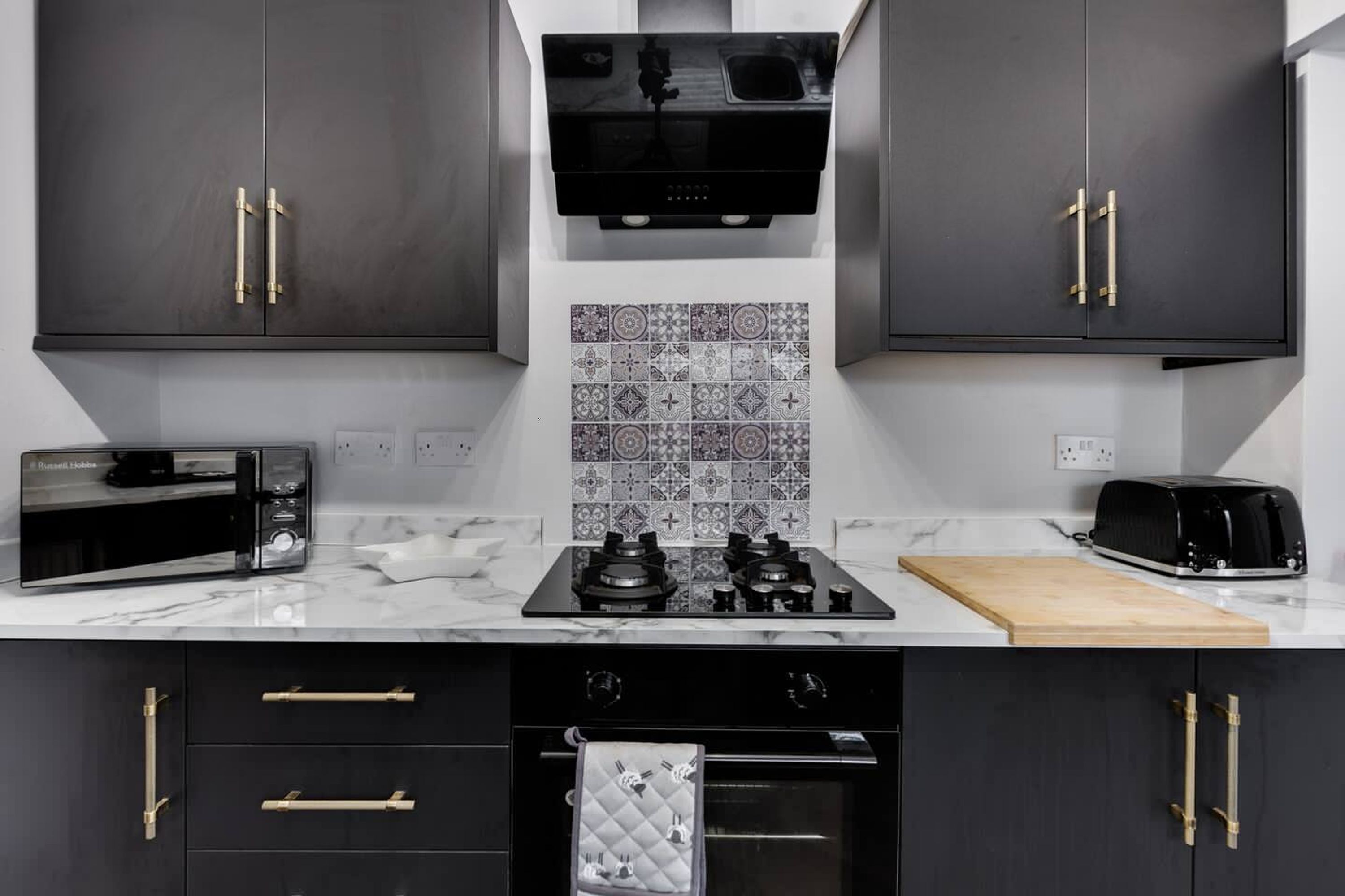 A modern kitchen with dark cabinets, a microwave, a toaster, and a stove.