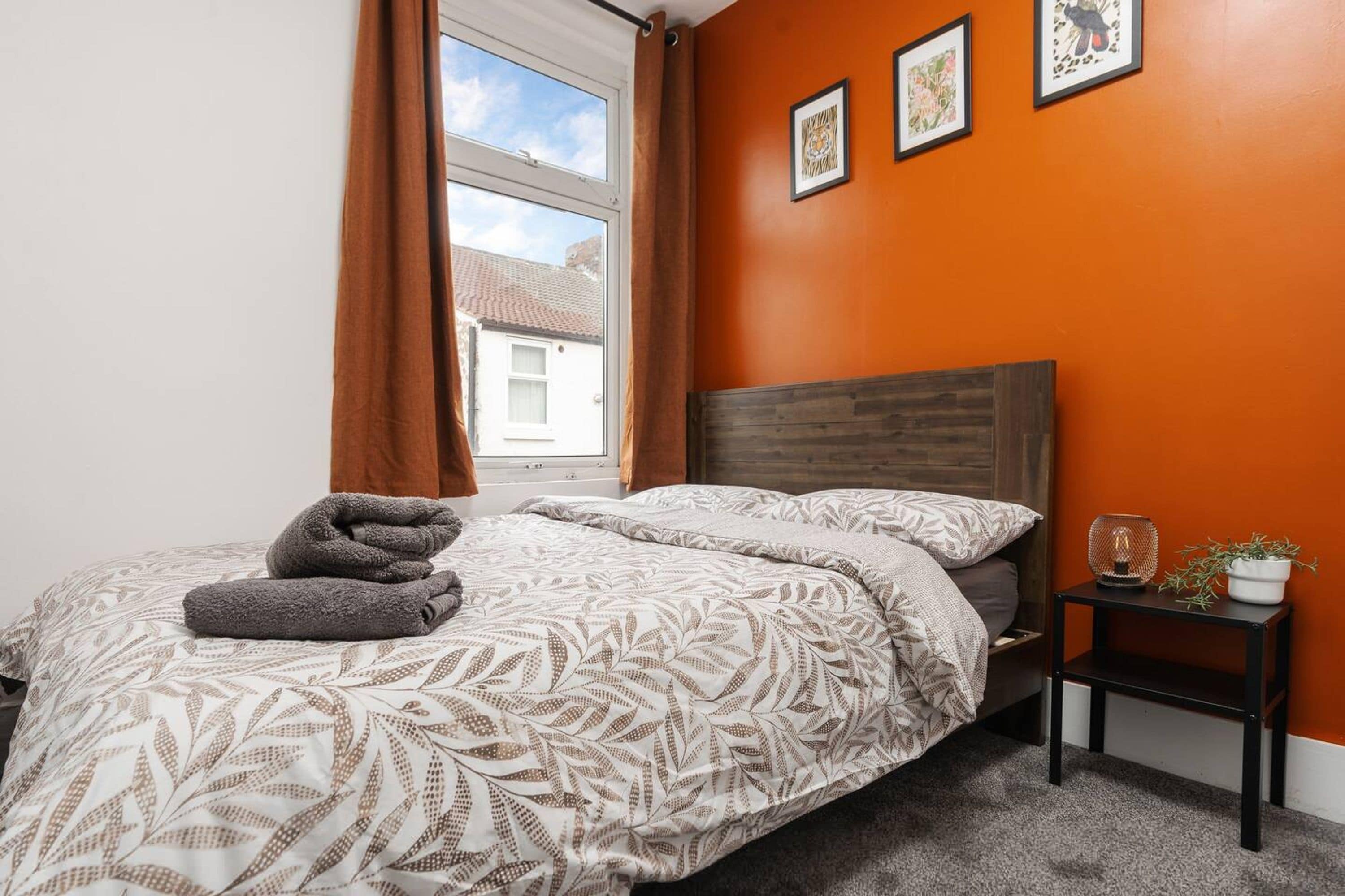 A bedroom with a bed, a nightstand, a window with curtains, and framed pictures on the wall.