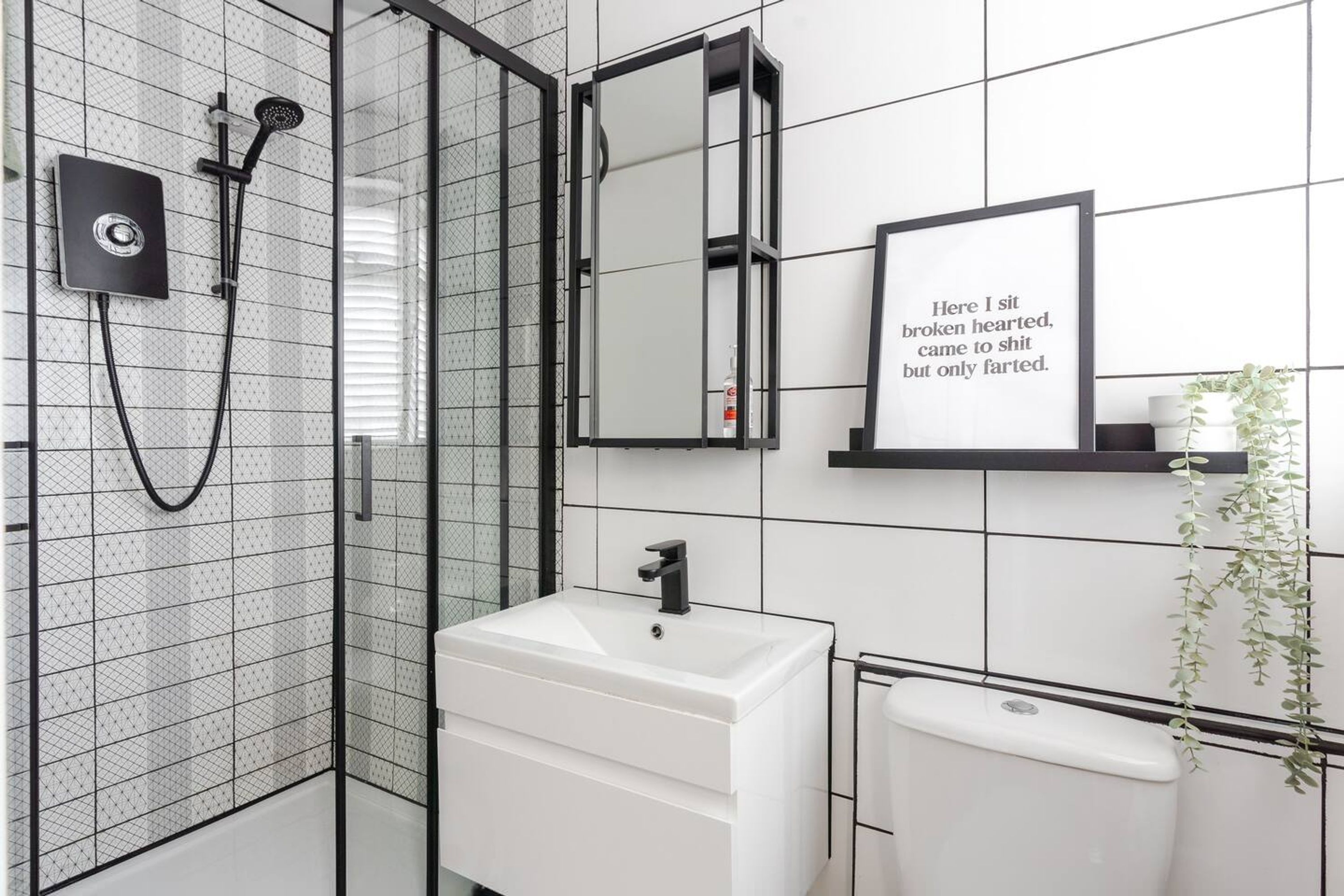 Moderni kylpyhuone, jossa on lasiseinällä varustettu suihku, valkoinen pesuallas, peili ja seinällä kehystetty inspiroiva sitaatti.