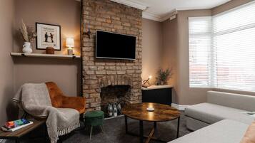 Una sala de estar con chimenea de ladrillo, un televisor de pantalla plana, un sofá, una mesa de centro y una silla.