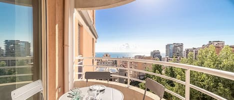 A balcony with a table set for two, overlooking a cityscape and the sea.
