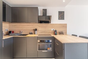 A modern kitchen with built-in appliances, a wooden countertop, and a dining area with chairs. - 1 Bedroom Renovated Near Monaco (Beausoleil)