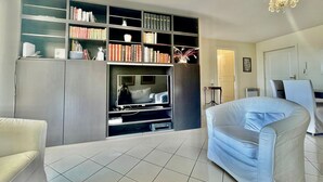 Una sala de estar con estantería, televisión, sofá blanco y candelabro.