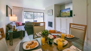 A dining area with a table set for breakfast, including croissants, fruit, and juice. There is a sofa and a television in the background. - 2BR Napa Getaway Side-by-side Condos Golf View (Napa)