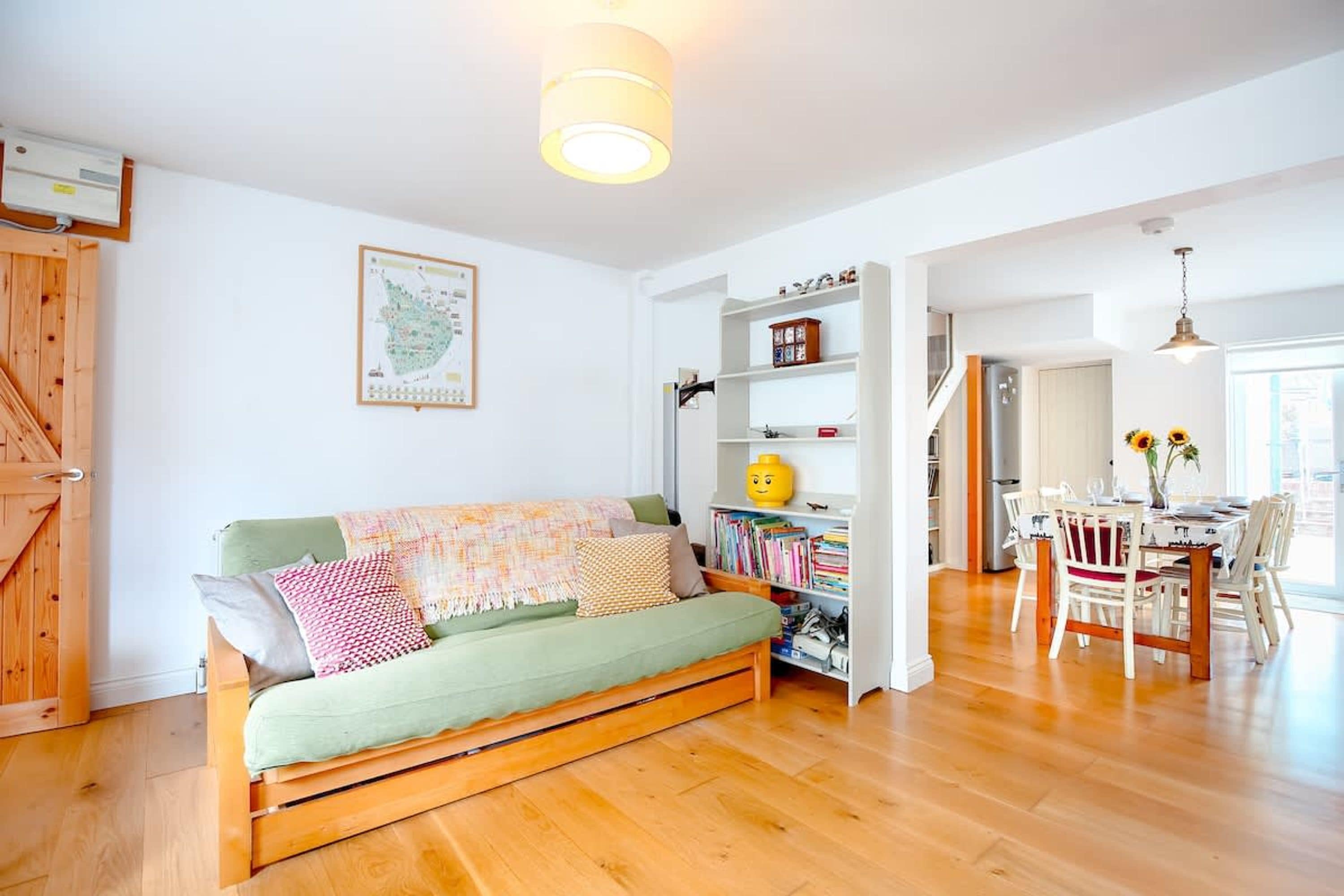 Una sala de estar acogedora con sofá, suelo de madera, una estantería y un comedor con sillas y mesa.