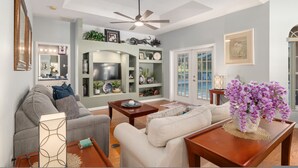 A living room with a grey sofa, a white sofa, a wooden coffee table, a ceiling fan, and a TV on a stand. - Villa Pearl 4-bedroom Poolhome Close To Ocala (Inverness)