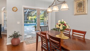 A dining area with a wooden table, chairs, a vase of flowers, a chandelier, and a view of a pool through glass doors. - Villa Pearl 4-bedroom Poolhome Close To Ocala (Inverness)