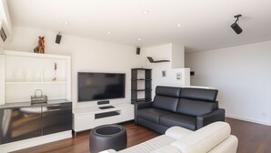 A modern living room with a flat-screen TV, a black leather sofa, a white sofa, and a wooden floor. - Stunning Renovated 1-bedroom Breathtaking View (Beausoleil)