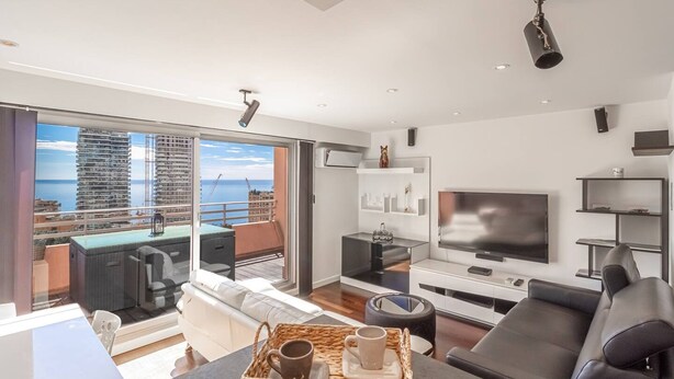 A modern living room with a large TV, comfortable seating, a dining area, and a balcony with a view of the city. - Stunning Renovated 1-bedroom Breathtaking View (Beausoleil)