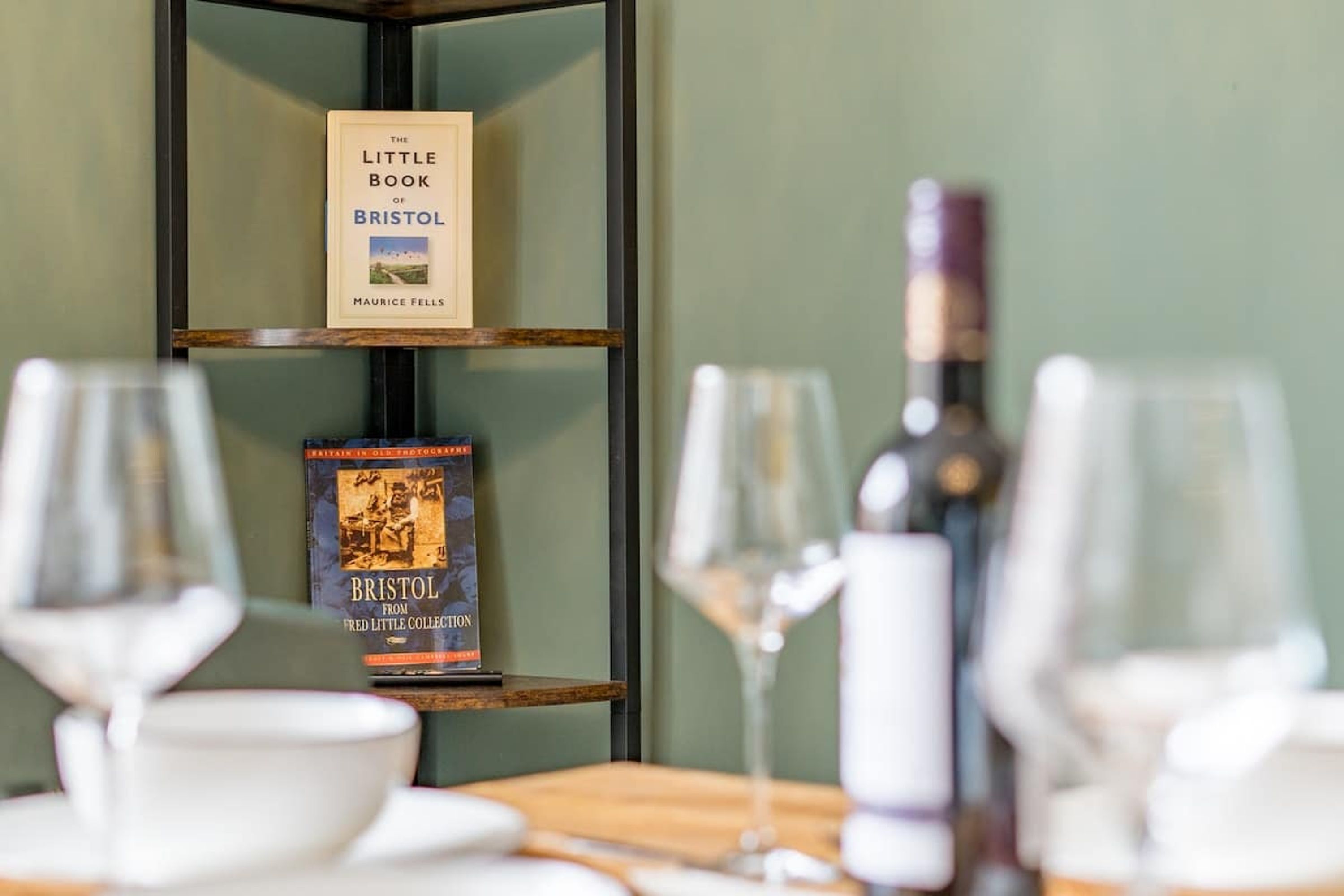 Una estantería con libros y una botella de vino sobre una mesa.