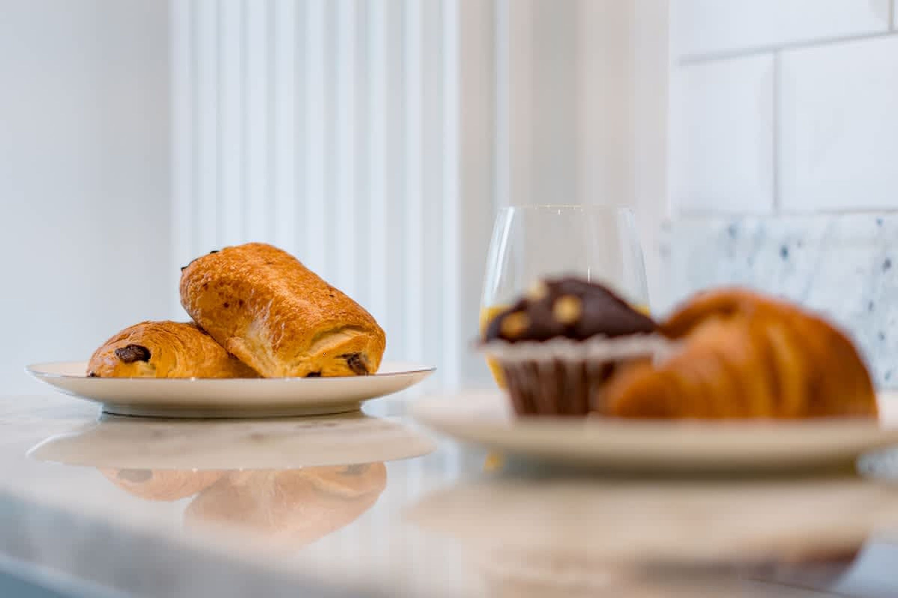 A plate with croissants and a glass of beverage on a reflective surface.