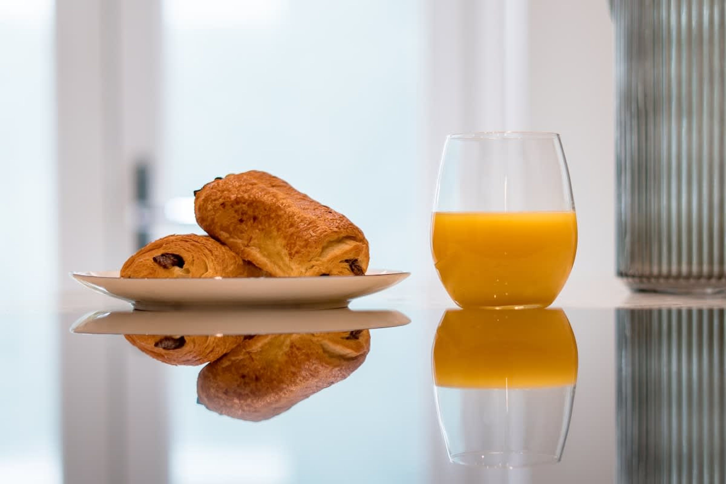 A plate with croissants and a glass of orange juice on a reflective surface.