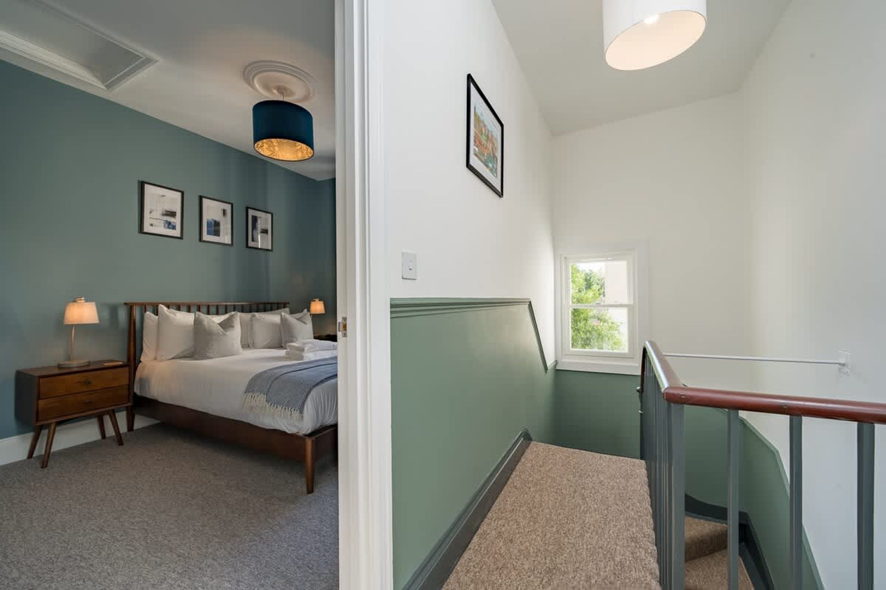 Un dormitorio con cama, mesita de noche, lámpara y cuadros en la pared.