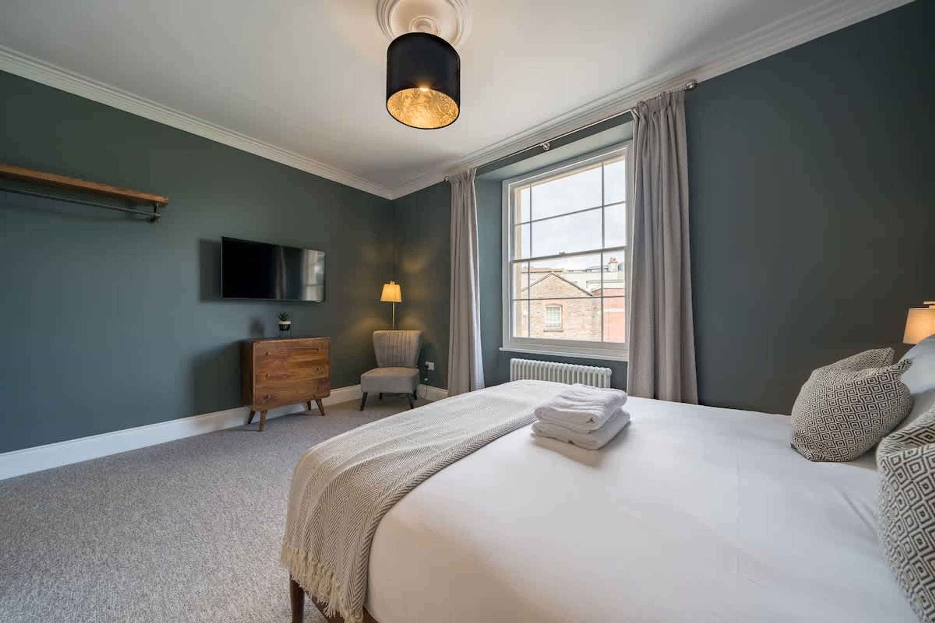 Une chambre à coucher avec un lit, une télévision, une chaise, une commode et une fenêtre.