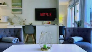 A modern living room with a flat-screen TV displaying 'NETFLIX,' a sofa, a coffee table, and a dining area with a white cabinet and a microwave. - Elegant Retreat Near Monaco Private Terrace (Beausoleil)