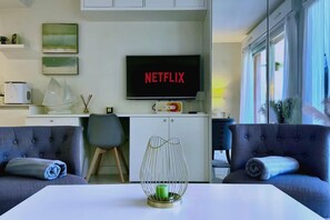 A modern living room with a flat-screen TV displaying 'NETFLIX,' a sofa, a coffee table, and a dining area with a white cabinet and a microwave. - Elegant Retreat Near Monaco Private Terrace (Beausoleil)