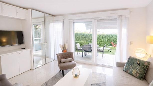 A modern living room with a flat-screen TV, a sofa, a coffee table, and a sliding glass door leading to an outdoor patio with a dining area. - Elegant Retreat Near Monaco Private Terrace (Beausoleil)