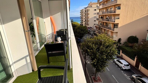 Un balcón con césped artificial, una mesa y sillas, con vista a una calle con coches y edificios.