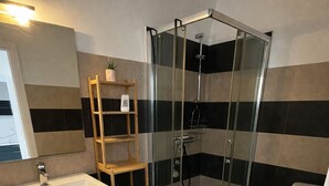 Un baño con ducha de vidrio, un lavabo blanco, un estante de madera y un inodoro.