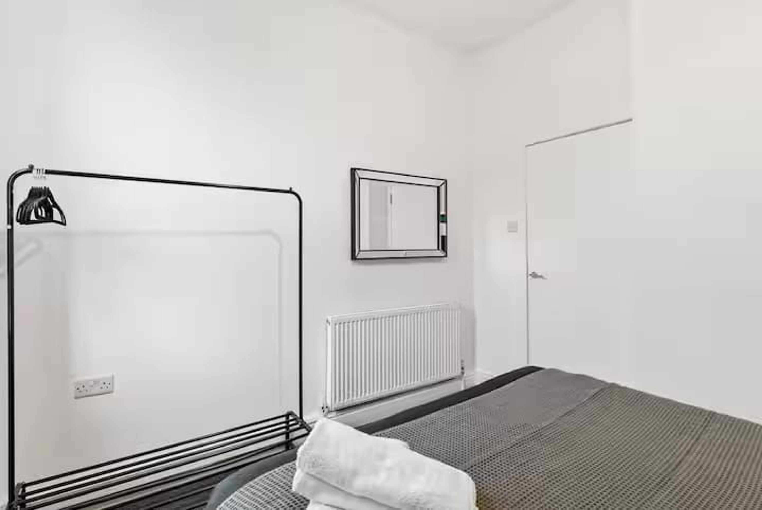 Una habitación con cama, radiador, espejo y puerta.