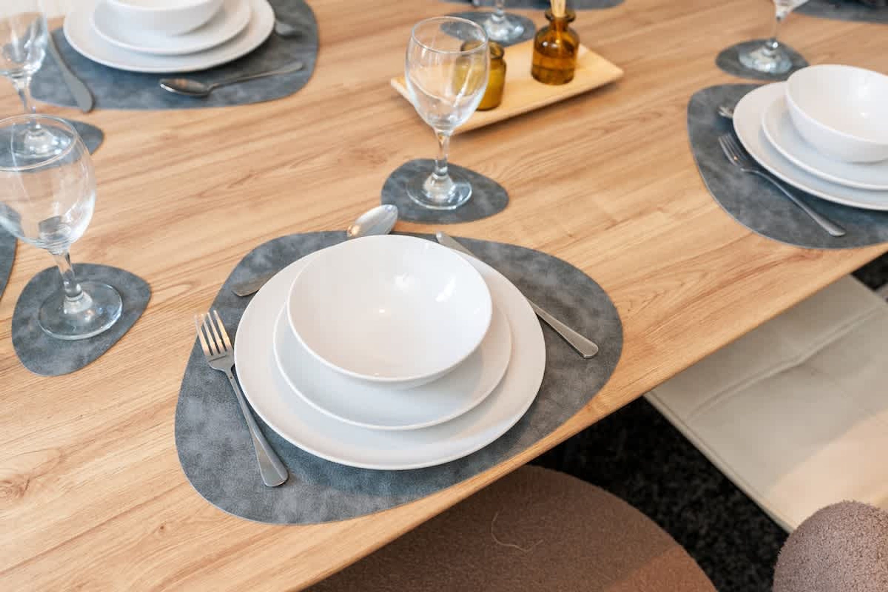 A dining table set with plates, cutlery, and glasses, with a wooden table and grey placemats.
