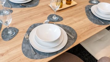 A dining table set with plates, cutlery, and glasses, with a wooden table and grey placemats.