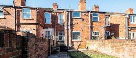 A narrow alleyway between terraced houses with brick walls, a metal gate, and a concrete path.