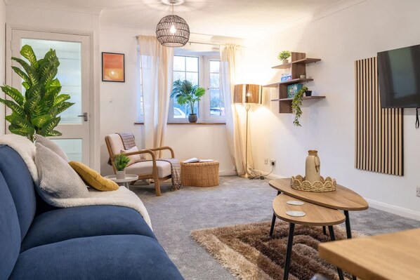 A living room with a sofa, a chair, a coffee table, a lamp, a TV, and a plant.