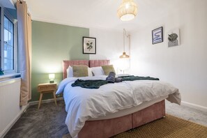 A bedroom with a bed, a bedside table, a lamp, and a window.