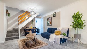 A living room with a staircase, a blue sofa, a small table, and a potted plant. - Perfect Booking 2 Bed Home in Hitchin (Hitchin)