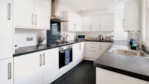 A modern kitchen with white cabinetry, a black countertop, stainless steel appliances, and a built-in oven. - Big Family Home Free Parking Fast Wifi Garden (Kingston Upon Thames)