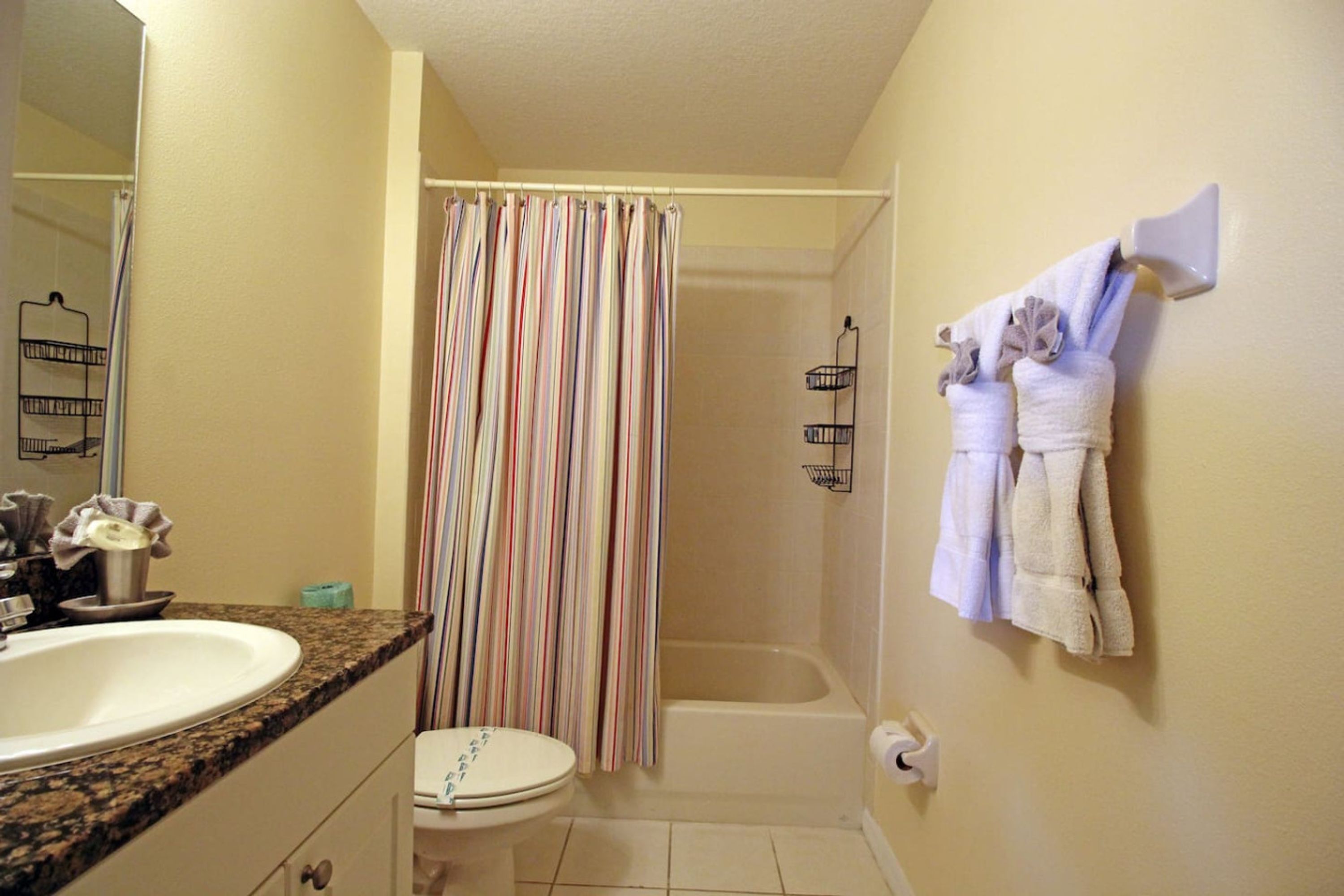 Ein Badezimmer mit Duschvorhang, Badewanne, Toilette, Waschbecken und Handtüchern, die an der Wand hängen.