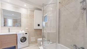 A modern bathroom with a glass-enclosed shower, a built-in washing machine, a toilet, and a large mirror. - Amazing Sea View T2- Near Monaco (Beausoleil)