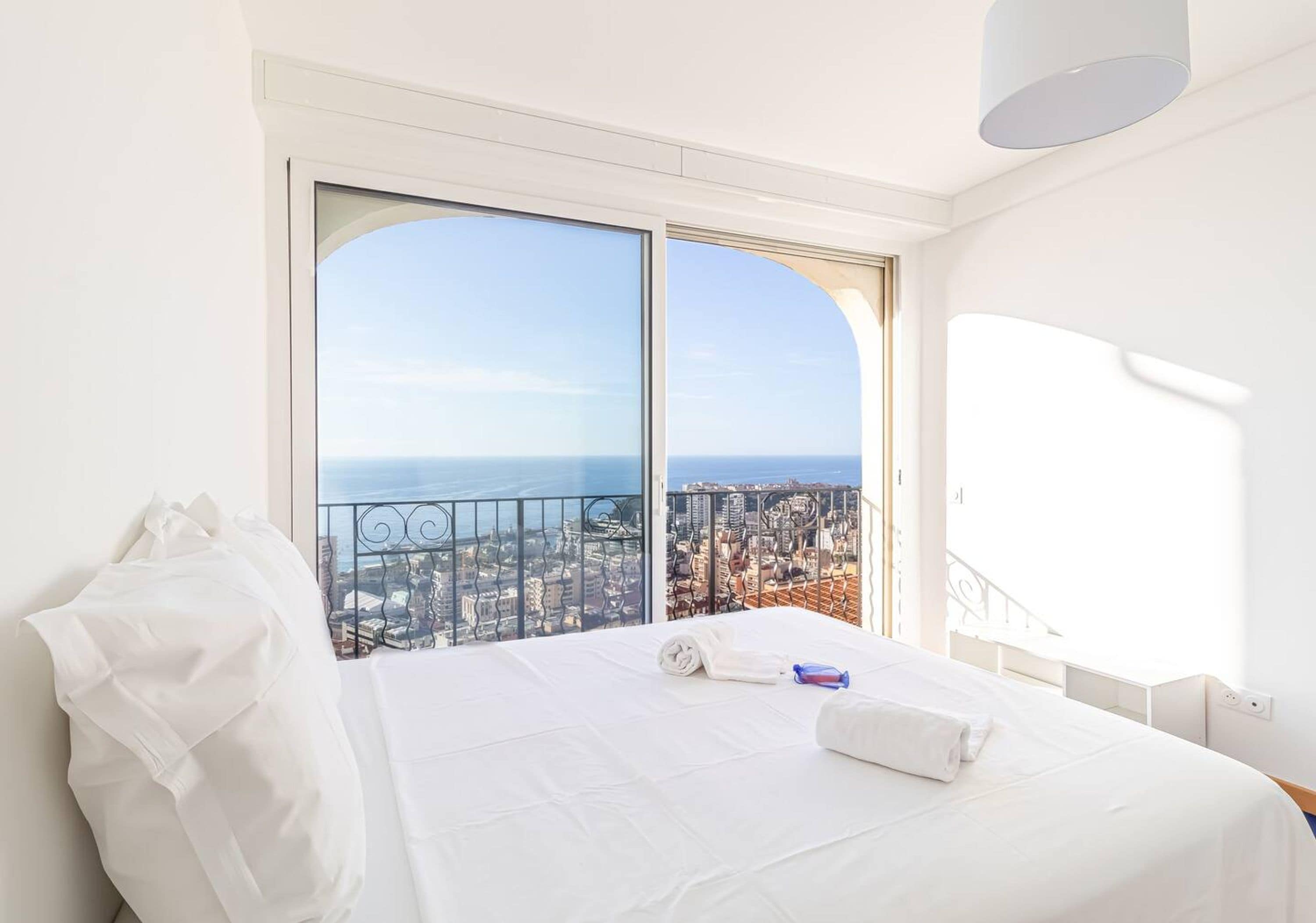 Ein Hotelzimmer mit einem großen Bett, Stadtblick und einem Balkon mit Geländer.