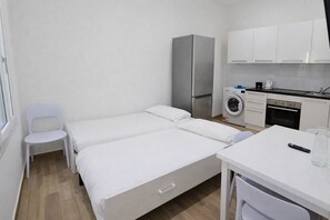 A small, clean room with a bed, a chair, a table, a washing machine, and a refrigerator. - Charming 1-bedroom Central Menton (Menton)