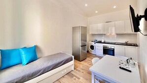 Um espaço compacto com sofá, mesa de jantar, cozinha compacta e máquina de lavar.